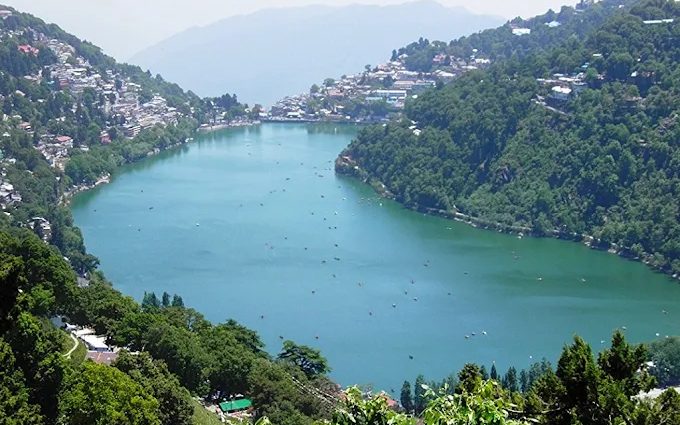 नैनी झील का ऊपर से दृश्य, किनारे बसा नैनीताल शहर और पानी पर नावें, शहर की कपल-होटल कीमत का केंद्र