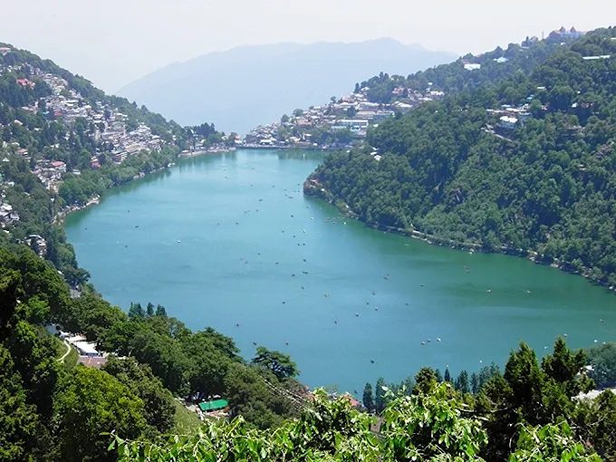 नैनी झील का ऊपर से दृश्य, किनारे बसा नैनीताल शहर और पानी पर नावें, शहर की कपल-होटल कीमत का केंद्र