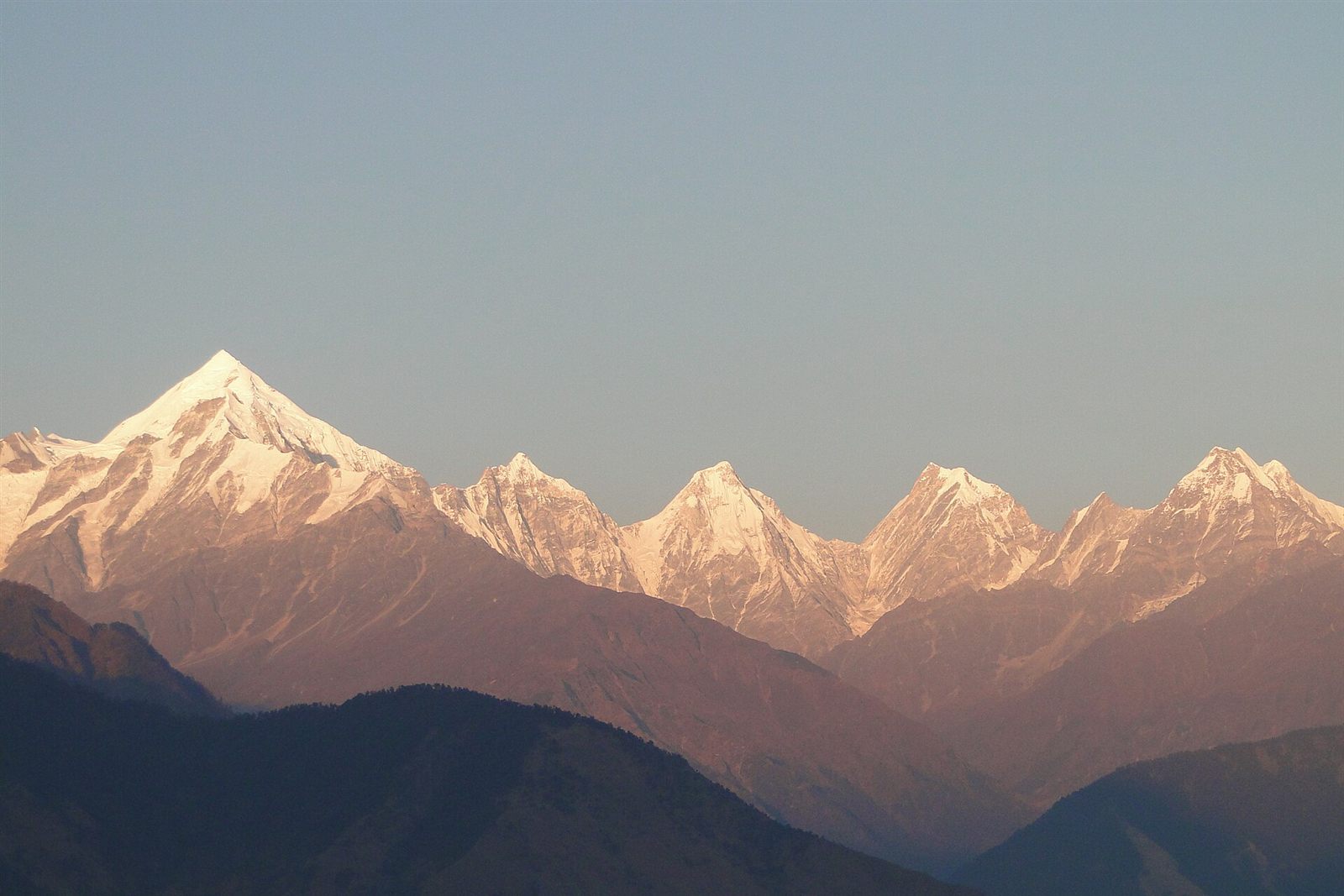 The Panchachuli peaks glowing pink at sunset above dark ridges, seen from Munsiyari